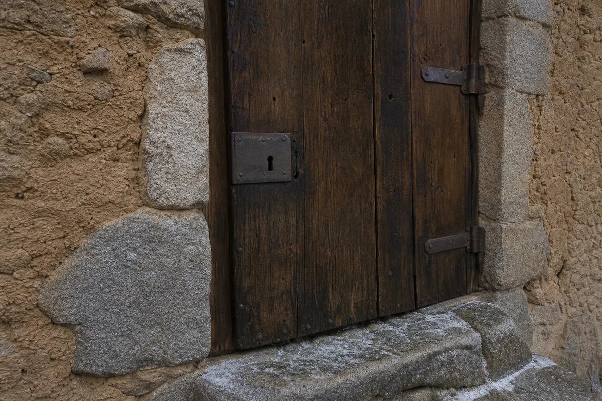 Porte ancienne en bois sombre encastrée dans un mur de pisé, serrure vue de près