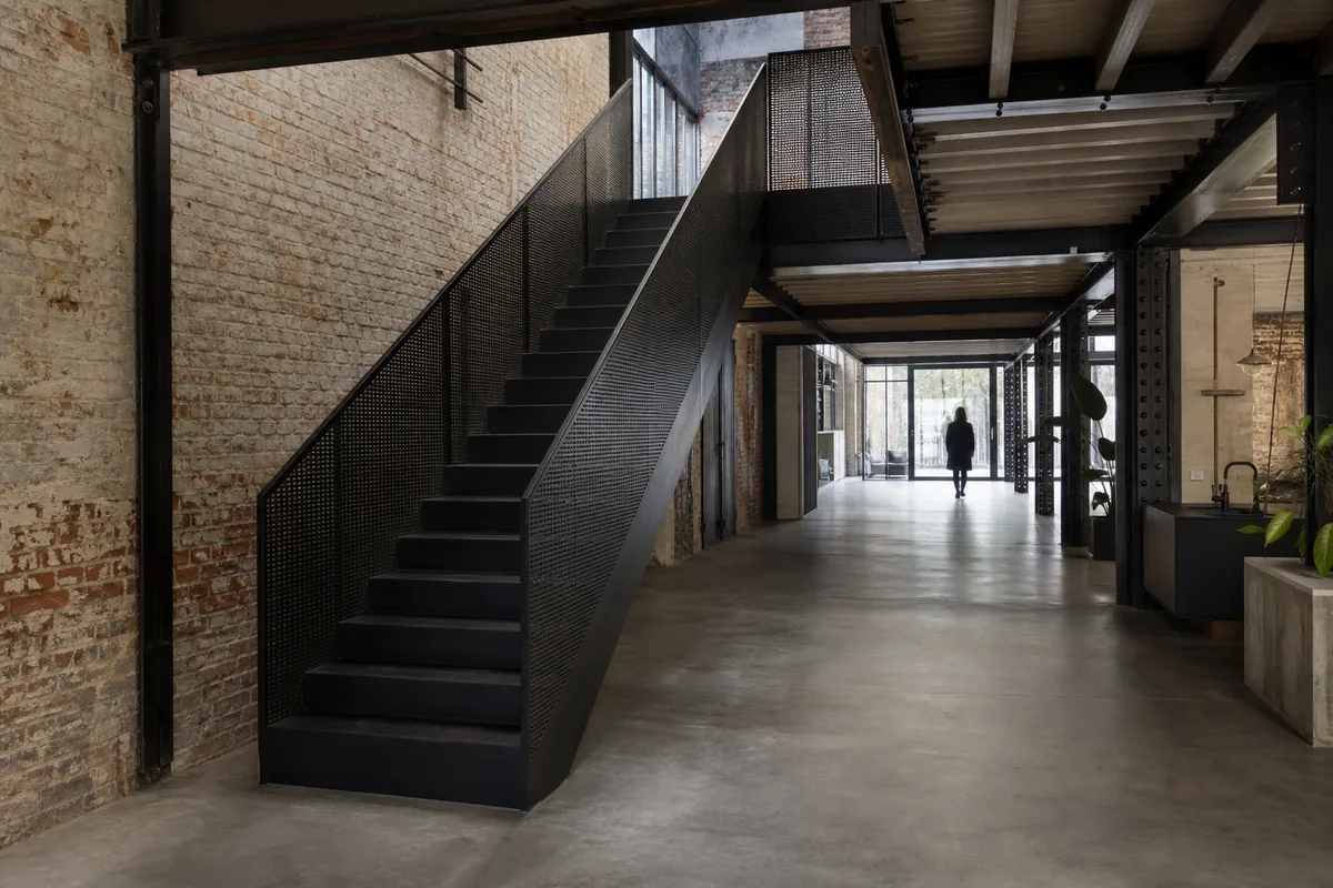 Escalier droit en acier avec remplissage en tôle perforée dans un loft en brique, lumière tamisée venant d’une verrière