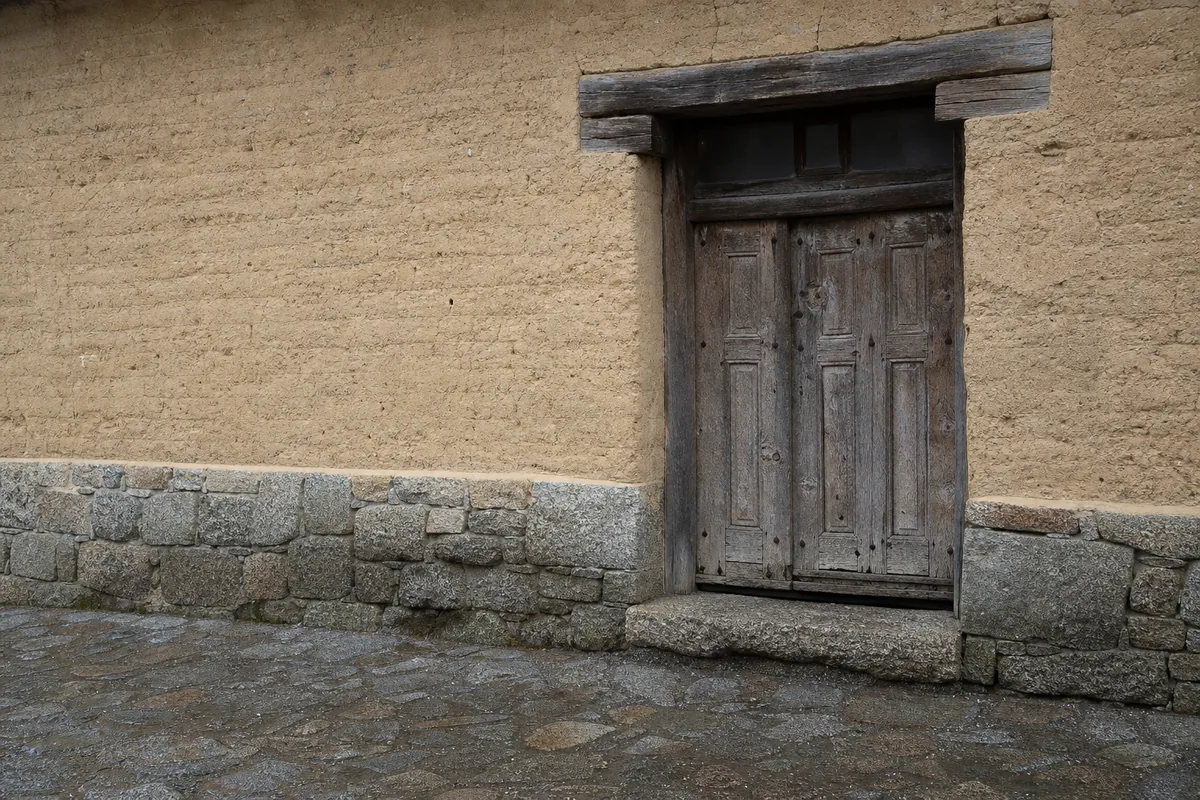 Porte d’entrée ancienne encastrée dans un mur de pisé, lumière grise de fin d’hiver