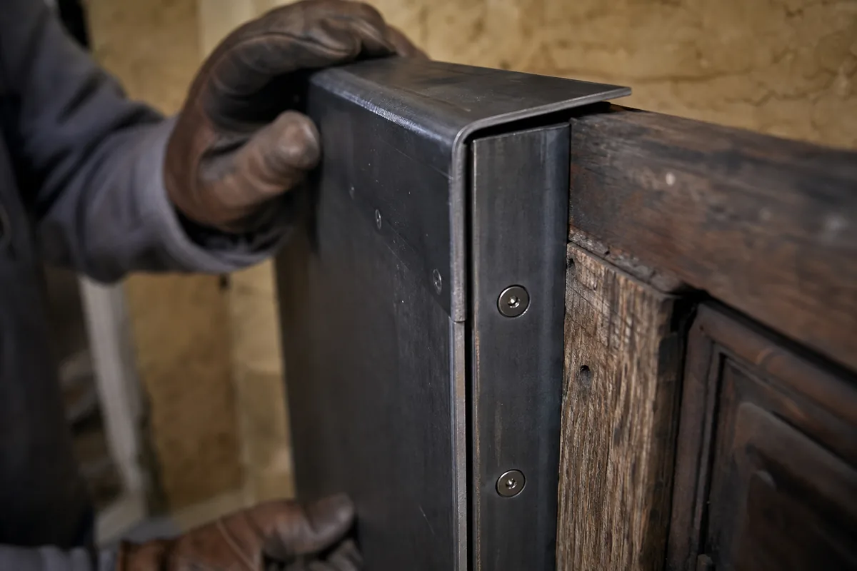 Cornière anti-pince en acier vissée sur le chant d’une porte blindée en applique